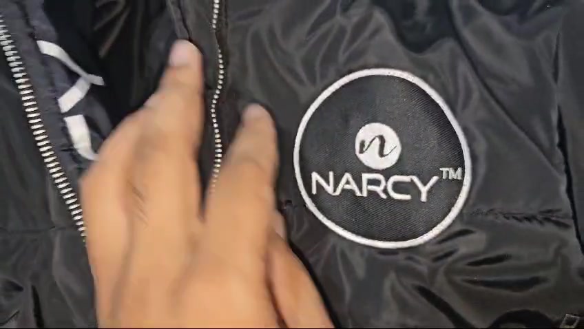 Close view of a black jacket with a circular Narcy logo while a hand opens the branded inner trim
