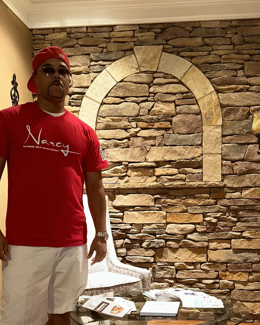 Adult man wearing a red Narcy wordmark T-shirt in a warmly lit interior editorial portrait