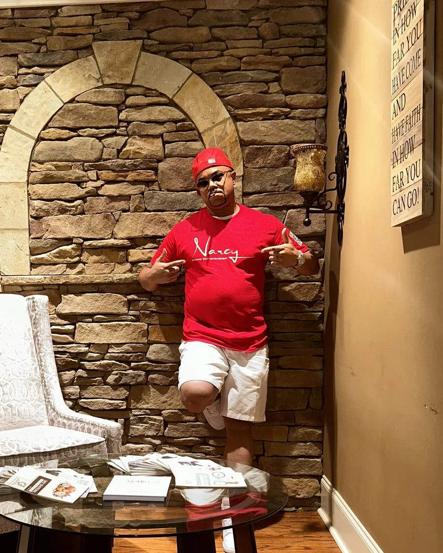 Adult man in a red Narcy wordmark T-shirt posing in an interior editorial scene