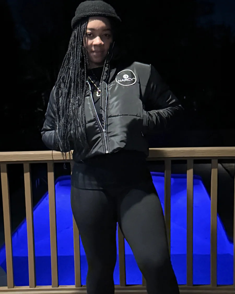 Adult woman outdoors at night wearing a black Narcy jacket with a circular chest patch