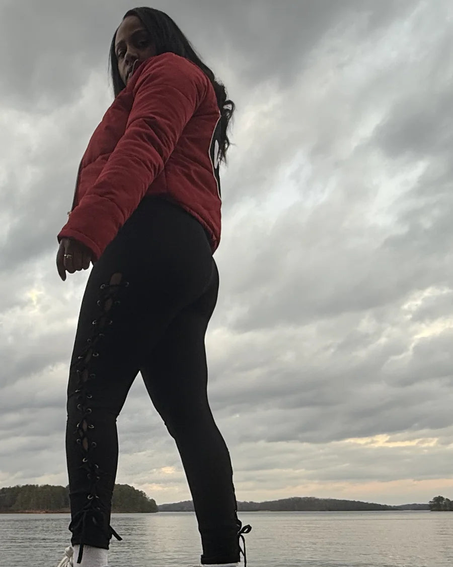 Adult woman near a lake wearing a red Narcy jacket with branded trim and a circular chest patch